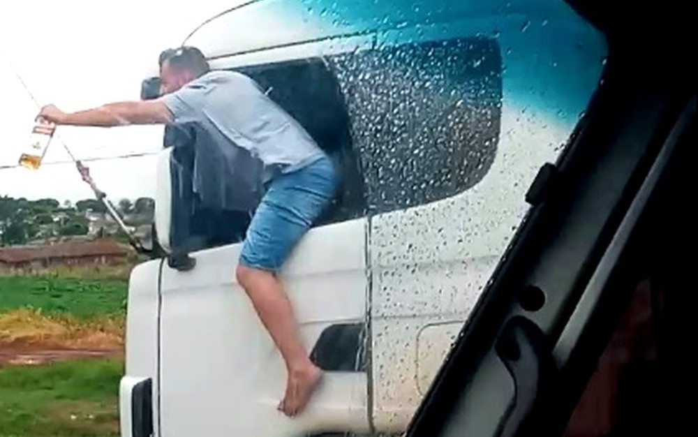 Caminhoneiro é filmado com corpo para fora de veículo com garrafa de bebida na mão enquanto dirige; VÍDEO